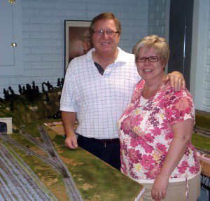 A man and woman standing next to a model train.