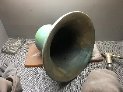 A green bell sitting on top of a wooden board.