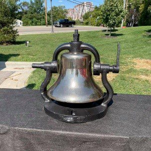 A bell sitting on top of a table in the middle of a park.