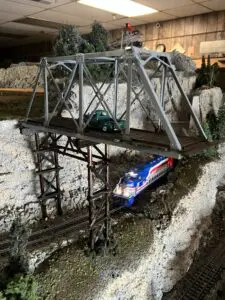 A train is on the tracks under an overpass.